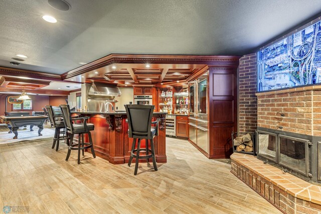 kitchen featuring wall oven, beverage cooler, light wood-type flooring, a brick fireplace, and pool table