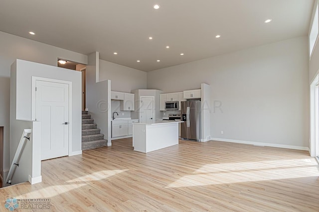 kitchen with a towering ceiling, a center island, light hardwood / wood-style floors, and stainless steel appliances