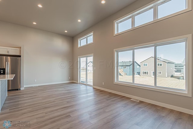 unfurnished living room with a healthy amount of sunlight, a high ceiling, and light hardwood / wood-style flooring