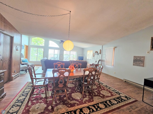 dining space featuring a textured ceiling, a baseboard radiator, wood-type flooring, and vaulted ceiling