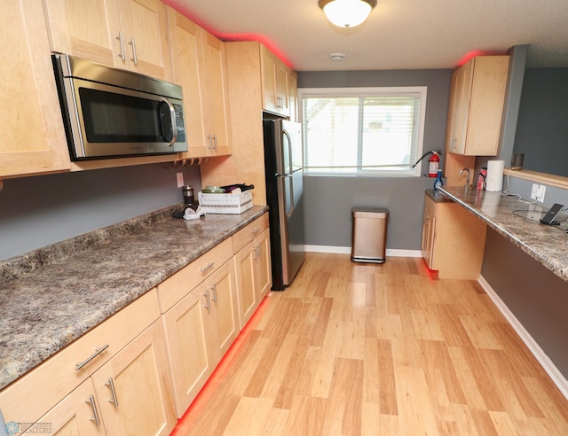 kitchen with dark stone counters, light hardwood / wood-style flooring, light brown cabinetry, and stainless steel appliances