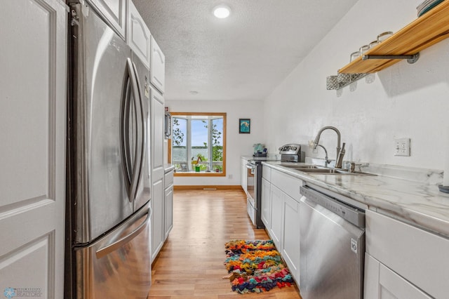 kitchen featuring light hardwood / wood-style flooring, white cabinetry, appliances with stainless steel finishes, sink, and a textured ceiling