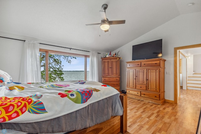 bedroom with ceiling fan, light wood-type flooring, a water view, and lofted ceiling