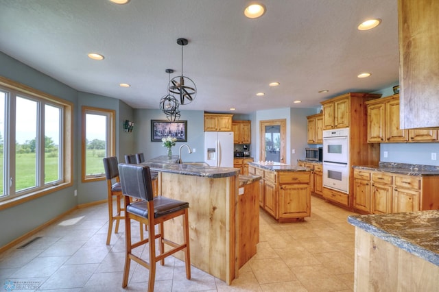 kitchen featuring decorative light fixtures, white appliances, a kitchen island with sink, and light tile floors