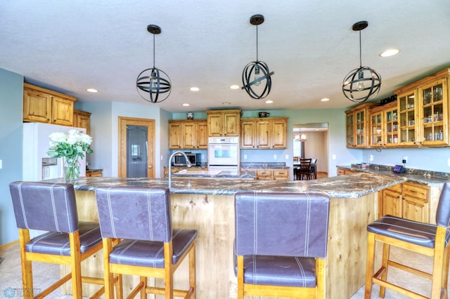 kitchen featuring white appliances, a kitchen island with sink, pendant lighting, sink, and a kitchen bar