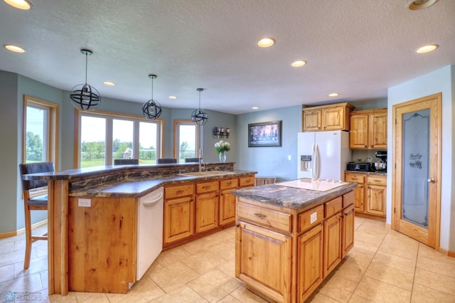 kitchen featuring sink, an island with sink, white appliances, and light tile flooring