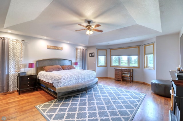 bedroom featuring light hardwood / wood-style floors, a textured ceiling, ceiling fan, and a raised ceiling