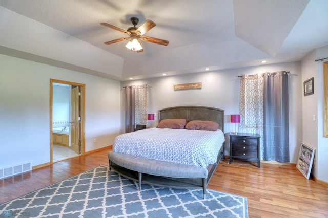 bedroom featuring hardwood / wood-style floors, connected bathroom, ceiling fan, and a tray ceiling