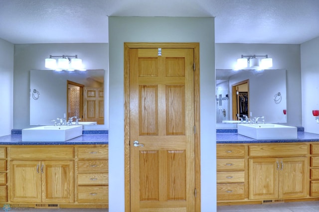 bathroom featuring dual bowl vanity, tile flooring, and a textured ceiling