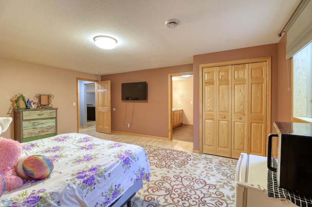 bedroom featuring a closet, a textured ceiling, light wood-type flooring, and ensuite bath