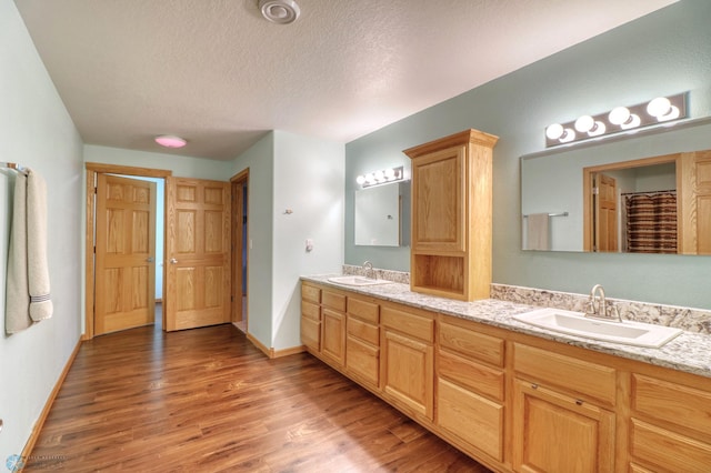 bathroom with double sink vanity, hardwood / wood-style flooring, and a textured ceiling