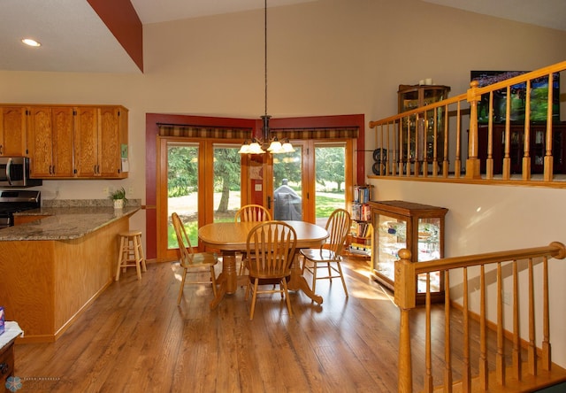 dining area with hardwood / wood-style flooring, a notable chandelier, and high vaulted ceiling