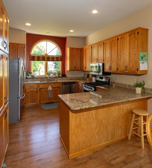 kitchen featuring appliances with stainless steel finishes, sink, light stone countertops, kitchen peninsula, and hardwood / wood-style flooring