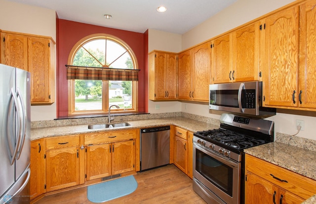 kitchen with sink, stainless steel appliances, light hardwood / wood-style floors, and light stone counters