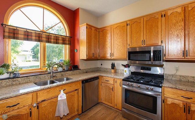 kitchen with sink, appliances with stainless steel finishes, light stone countertops, and light hardwood / wood-style floors