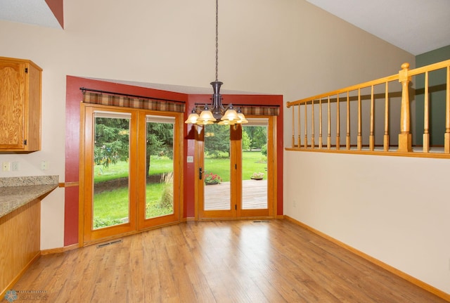 unfurnished dining area with high vaulted ceiling, light wood-type flooring, and an inviting chandelier