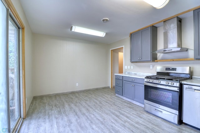 kitchen featuring white dishwasher, wall chimney range hood, stainless steel gas range oven, light hardwood / wood-style flooring, and gray cabinets