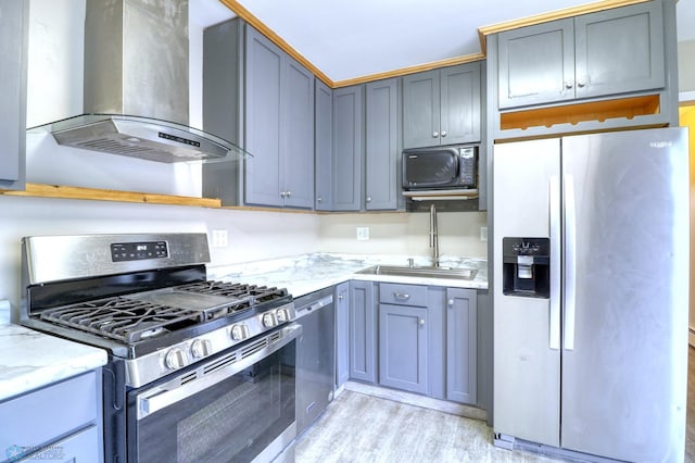 kitchen featuring light stone countertops, light wood-type flooring, appliances with stainless steel finishes, wall chimney exhaust hood, and sink