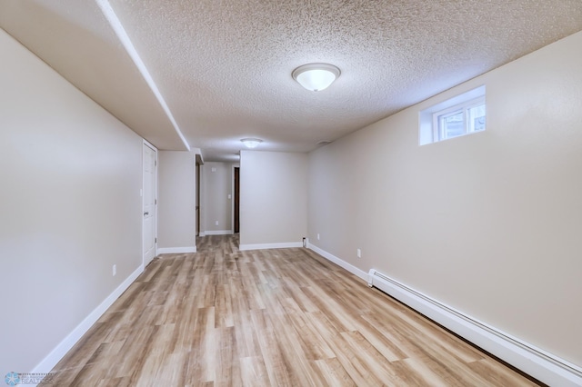 basement with a baseboard heating unit, light hardwood / wood-style floors, and a textured ceiling