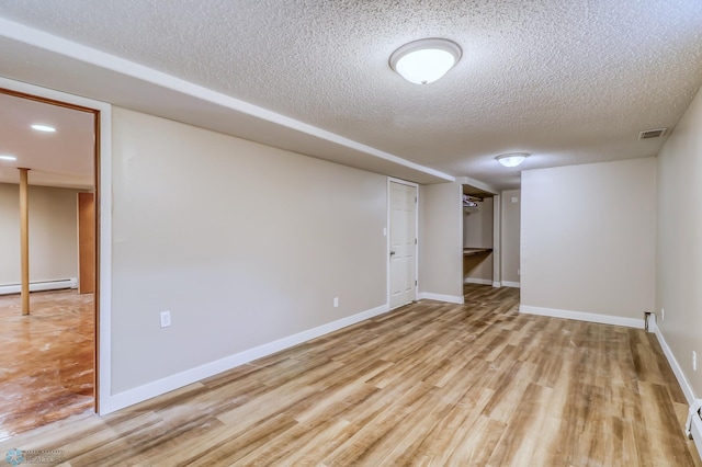 basement featuring light hardwood / wood-style flooring, a textured ceiling, and a baseboard radiator