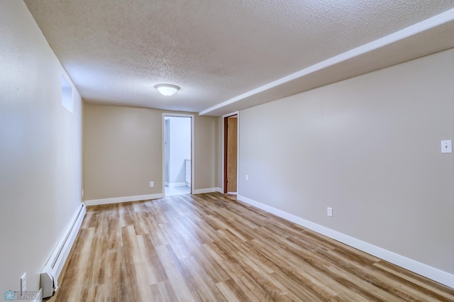 spare room featuring a baseboard heating unit, light hardwood / wood-style flooring, and a textured ceiling