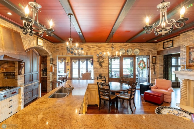 kitchen with beam ceiling, pendant lighting, dark wood-type flooring, brick wall, and sink