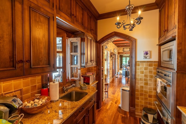 kitchen featuring hardwood / wood-style floors, stainless steel microwave, ornamental molding, light stone countertops, and sink