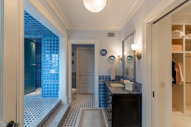 bathroom with tiled shower, vanity with extensive cabinet space, toilet, tile floors, and ornamental molding