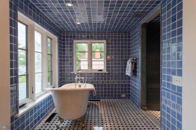 bathroom featuring a wealth of natural light, tile walls, a bath, and tile floors