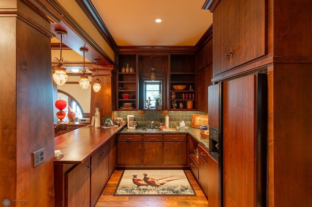 kitchen with crown molding, light wood-type flooring, decorative light fixtures, paneled fridge, and backsplash