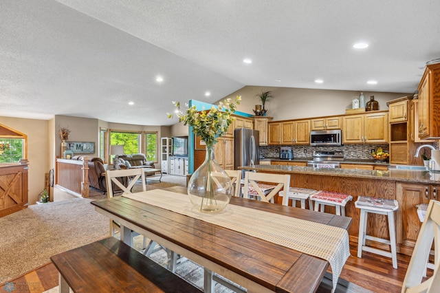 dining room with sink, a wealth of natural light, wood-type flooring, and vaulted ceiling