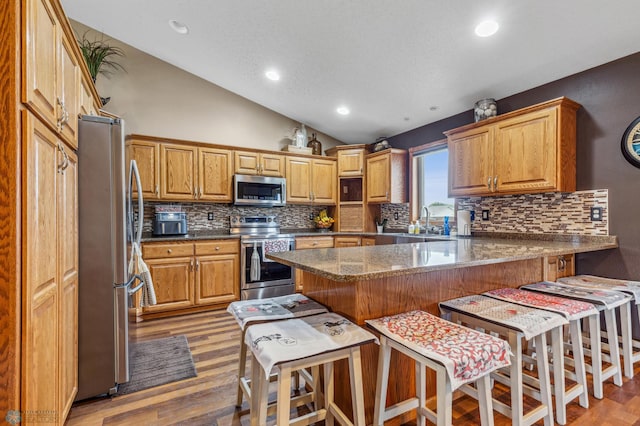 kitchen with stainless steel appliances, vaulted ceiling, backsplash, and light hardwood / wood-style flooring