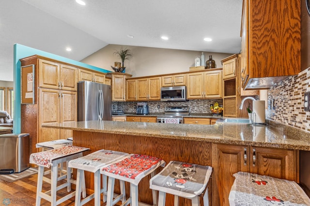 kitchen featuring light wood-type flooring, appliances with stainless steel finishes, kitchen peninsula, tasteful backsplash, and vaulted ceiling