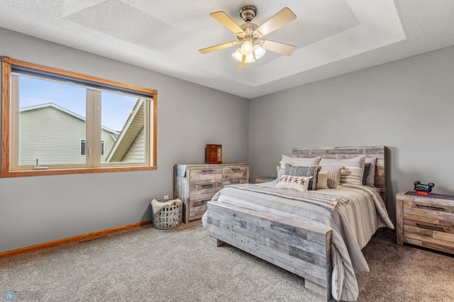 carpeted bedroom featuring a textured ceiling, ceiling fan, and a raised ceiling