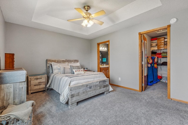 bedroom with ceiling fan, a spacious closet, a raised ceiling, carpet, and connected bathroom