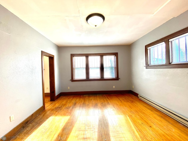 empty room with hardwood / wood-style floors, a wealth of natural light, and baseboard heating