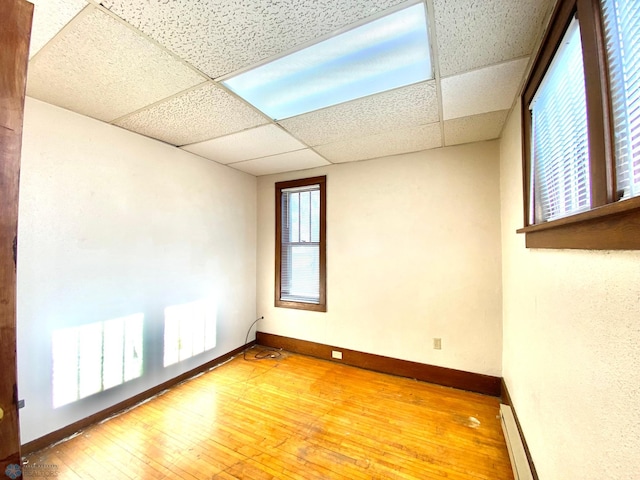 empty room featuring a baseboard heating unit, hardwood / wood-style floors, and a drop ceiling