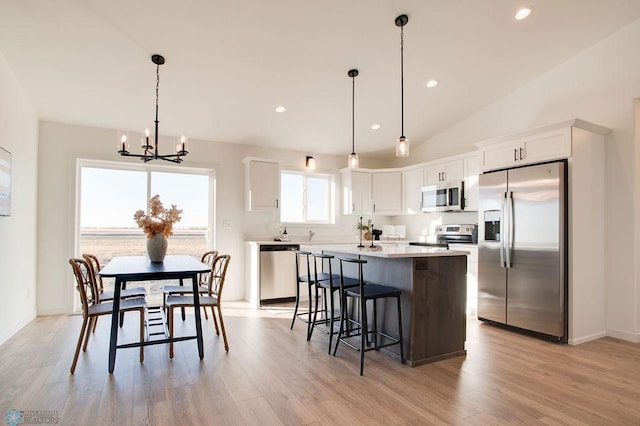 kitchen with a center island, light wood-type flooring, pendant lighting, appliances with stainless steel finishes, and lofted ceiling