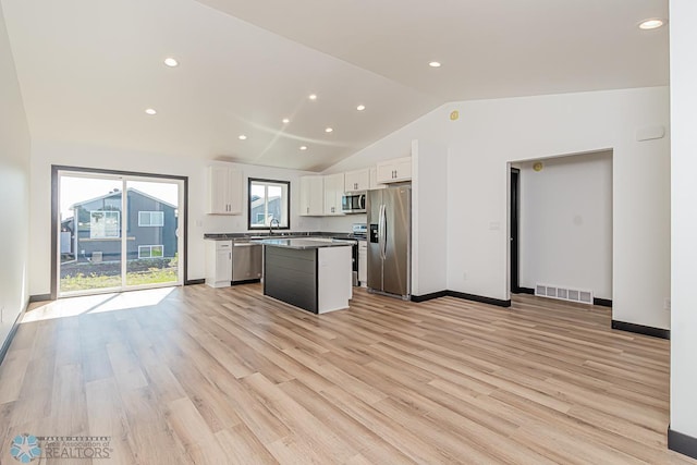 kitchen with lofted ceiling, a center island, light wood-type flooring, white cabinets, and appliances with stainless steel finishes