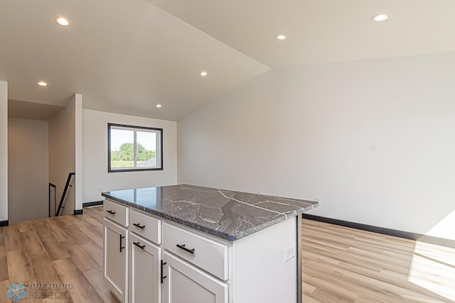 kitchen with light hardwood / wood-style floors, vaulted ceiling, dark stone countertops, a center island, and white cabinets