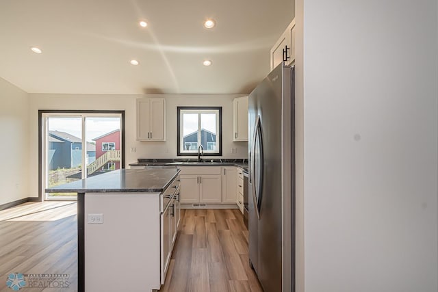 kitchen with light hardwood / wood-style floors, stainless steel fridge, a center island, sink, and white cabinetry