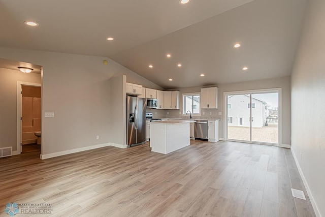 kitchen with a center island, light wood-type flooring, appliances with stainless steel finishes, white cabinets, and vaulted ceiling