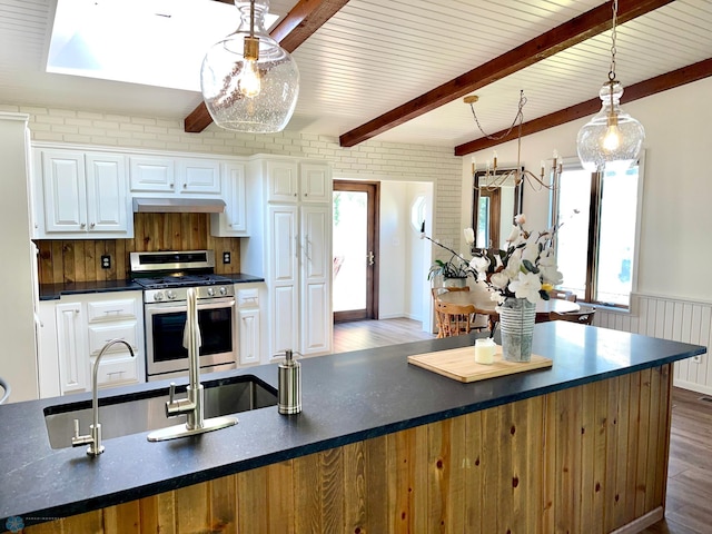 kitchen with decorative light fixtures, wood-type flooring, beam ceiling, gas stove, and white cabinets