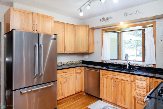 kitchen featuring appliances with stainless steel finishes, sink, light hardwood / wood-style flooring, and a textured ceiling