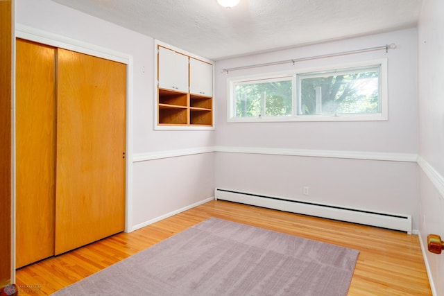 unfurnished bedroom with a textured ceiling, a closet, a baseboard radiator, and light wood-type flooring