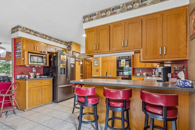 kitchen with appliances with stainless steel finishes, a breakfast bar area, light tile patterned floors, and backsplash