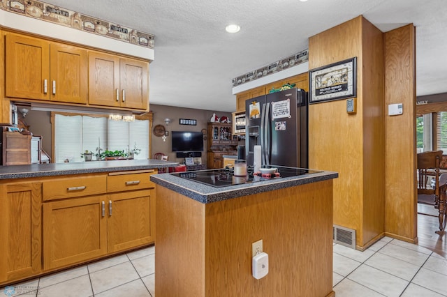 kitchen with light tile patterned flooring, black appliances, a kitchen island, and a textured ceiling