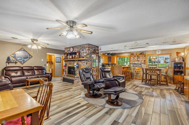 living room featuring wood-type flooring, a fireplace, ceiling fan, brick wall, and a textured ceiling