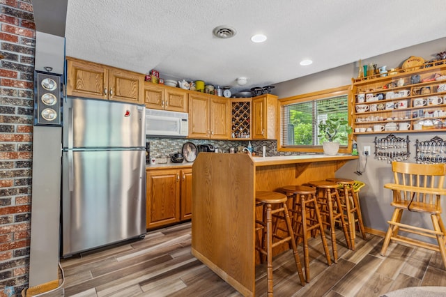 kitchen with stainless steel refrigerator, decorative backsplash, a textured ceiling, brick wall, and hardwood / wood-style flooring