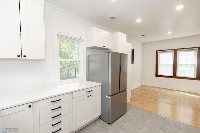 kitchen featuring crown molding, white cabinetry, stainless steel refrigerator, and light tile patterned floors